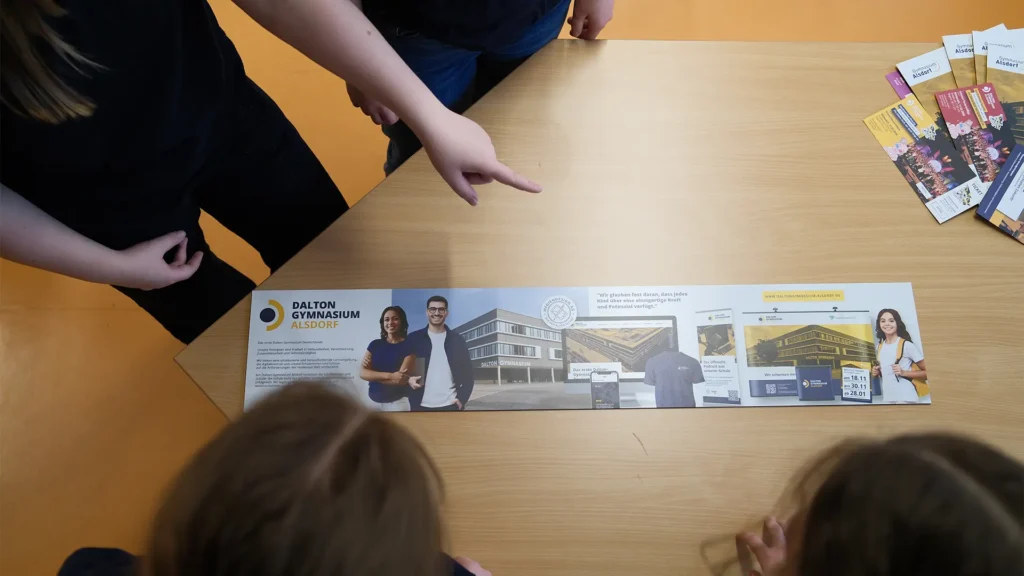 Mehrere Schülerinnen schauen sich einen ausgebreiteten Informationsflyer zum Dalton-Gymnasium an.
