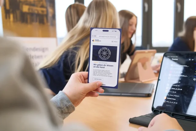 Schülerin hält eine Smartphone-Darstellung der Schulwebsite in der Hand.
