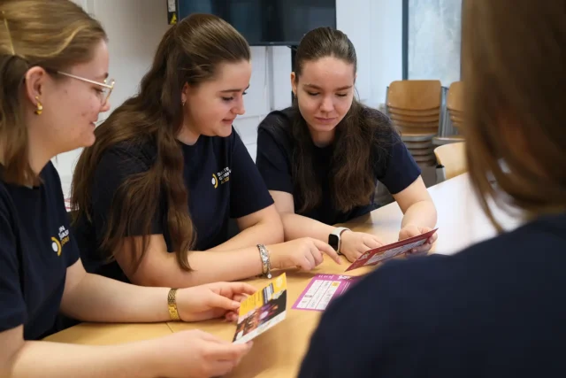 Schülerinnen arbeiten gemeinsam an Gestaltungsideen und betrachten Druckmaterialien.