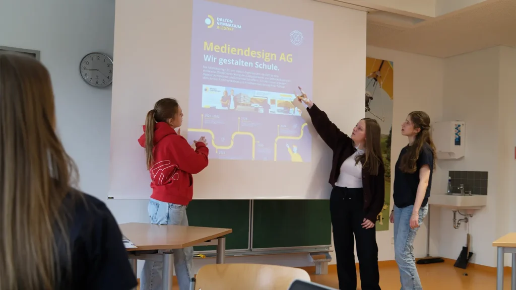 Schülerinnen präsentieren Ergebnisse der Mediendesign AG vor der Klasse.