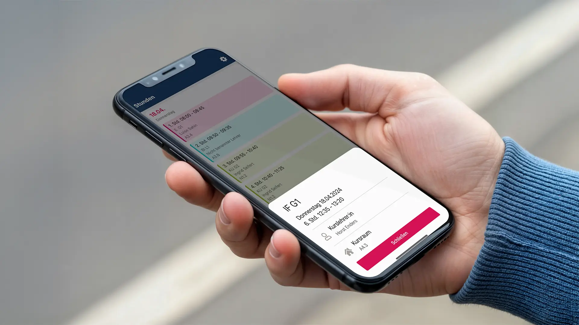 Hand hält ein Smartphone mit geöffneter AIXONE Eltern-App, die den Stundenplan und Details zu einer Unterrichtsstunde anzeigt.