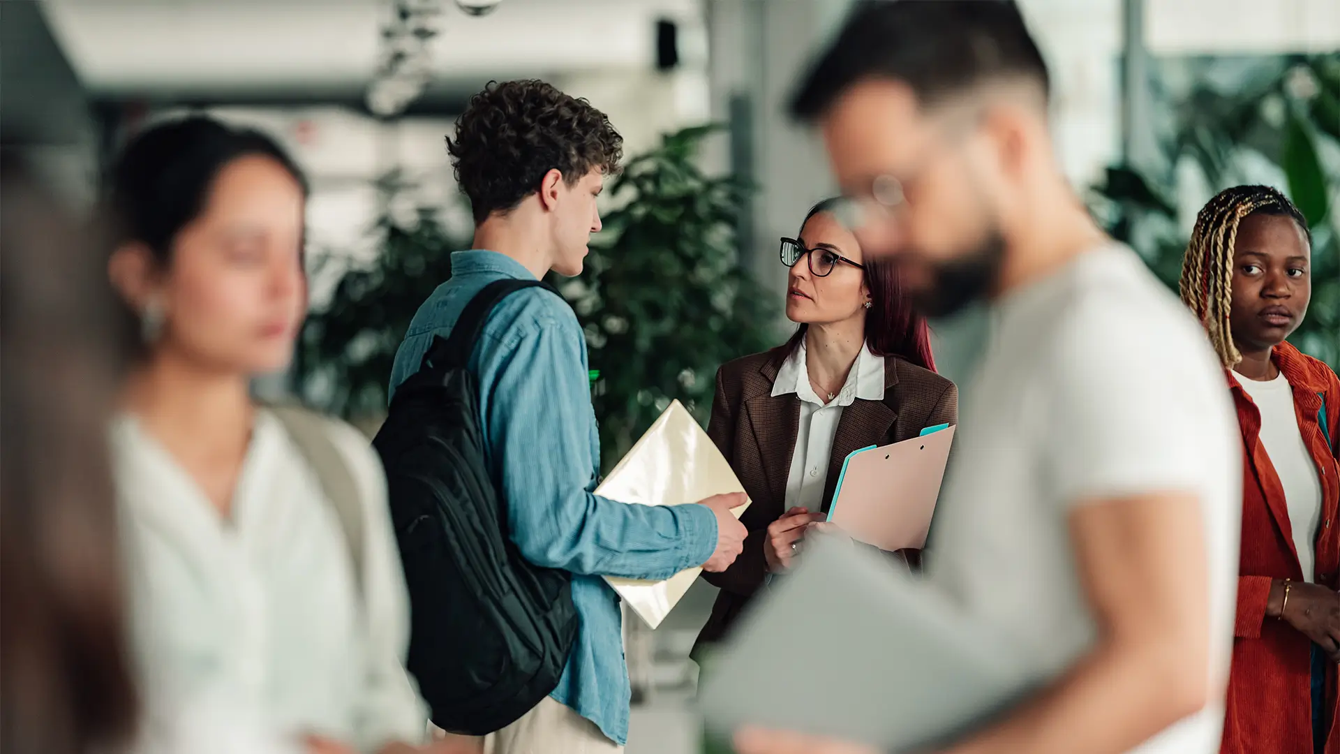 Schüler im Gespräch mit einer Beraterin in einem belebten Schulgebäude, umgeben von weiteren Personen.